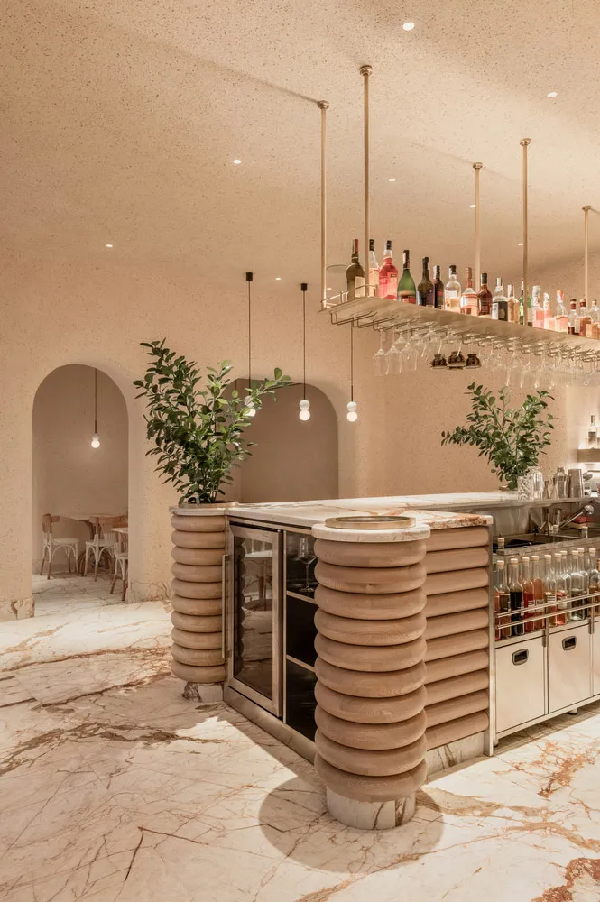 A modern bar area with a wooden counter, marble floor, and hanging wine bottles.