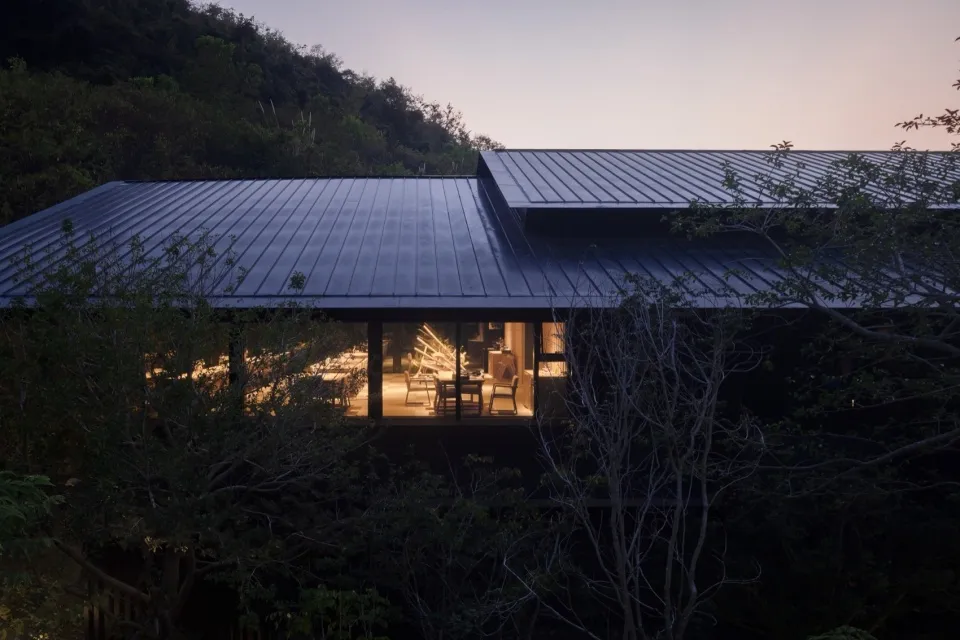 一棟擁有黑色金屬屋頂與大片玻璃窗的現代住宅。