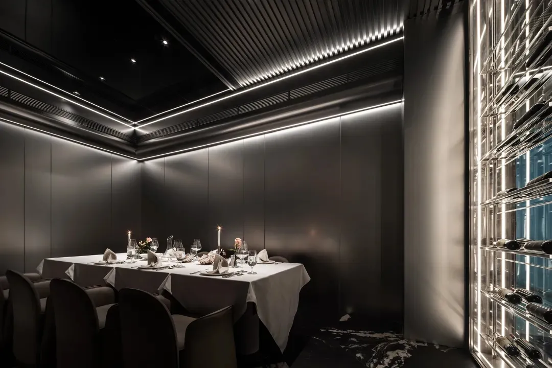 A sleek, modern restaurant dining room with metallic texture walls, illuminated by subtle LED lighting and featuring a dining