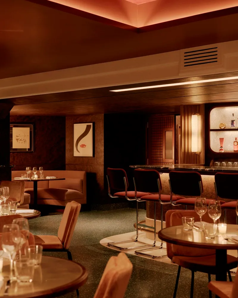 Contemporary restaurant bar with upholstered seating, tables, and barstools, featuring a warm, inviting ambiance created by f