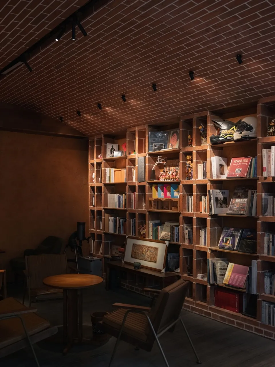 A cozy industrial-style reading room with brick walls and wooden furniture, featuring bookshelves filled with books and decor