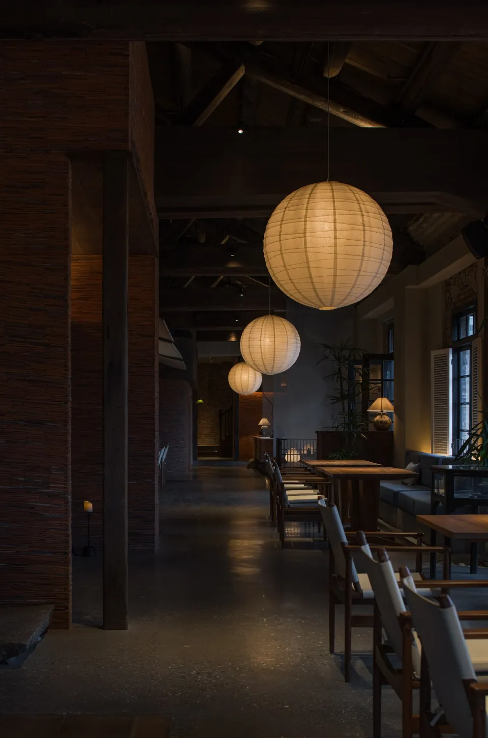 工業風餐廳內部,懸掛紙燈籠、木製座椅與混凝土地板。