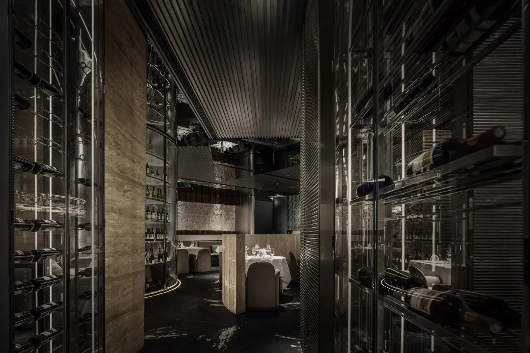 A modern industrial restaurant interior with metal shelving displaying bottles of wine and a dining area with tables and chai