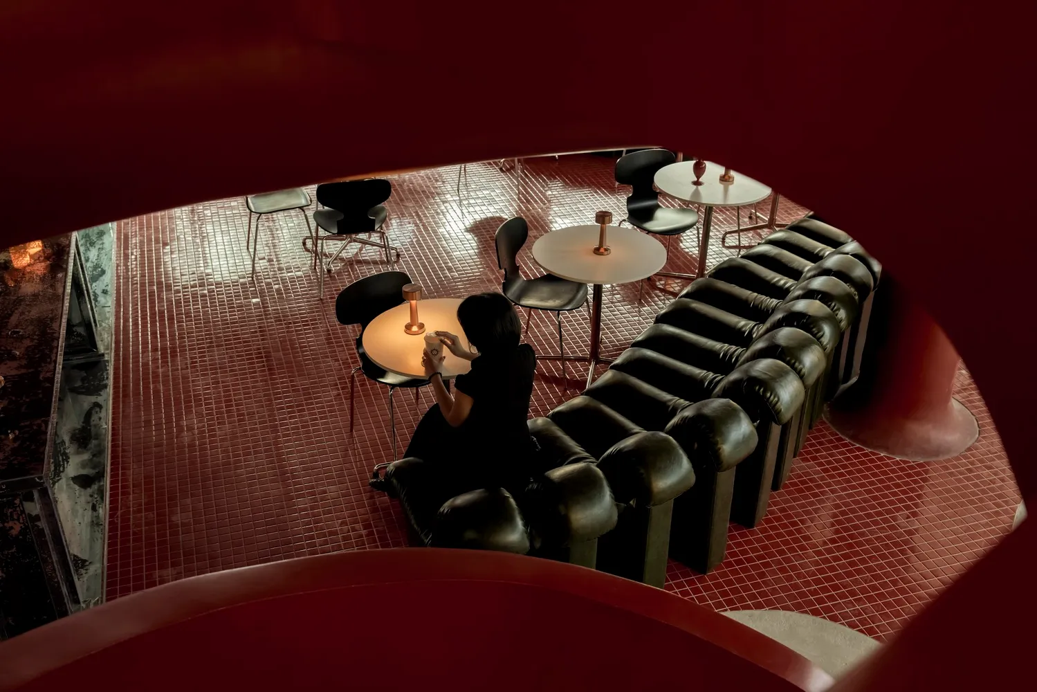 A modern cafeteria with black leather furniture and a metal floor, featuring a person sitting at a table with a drink.