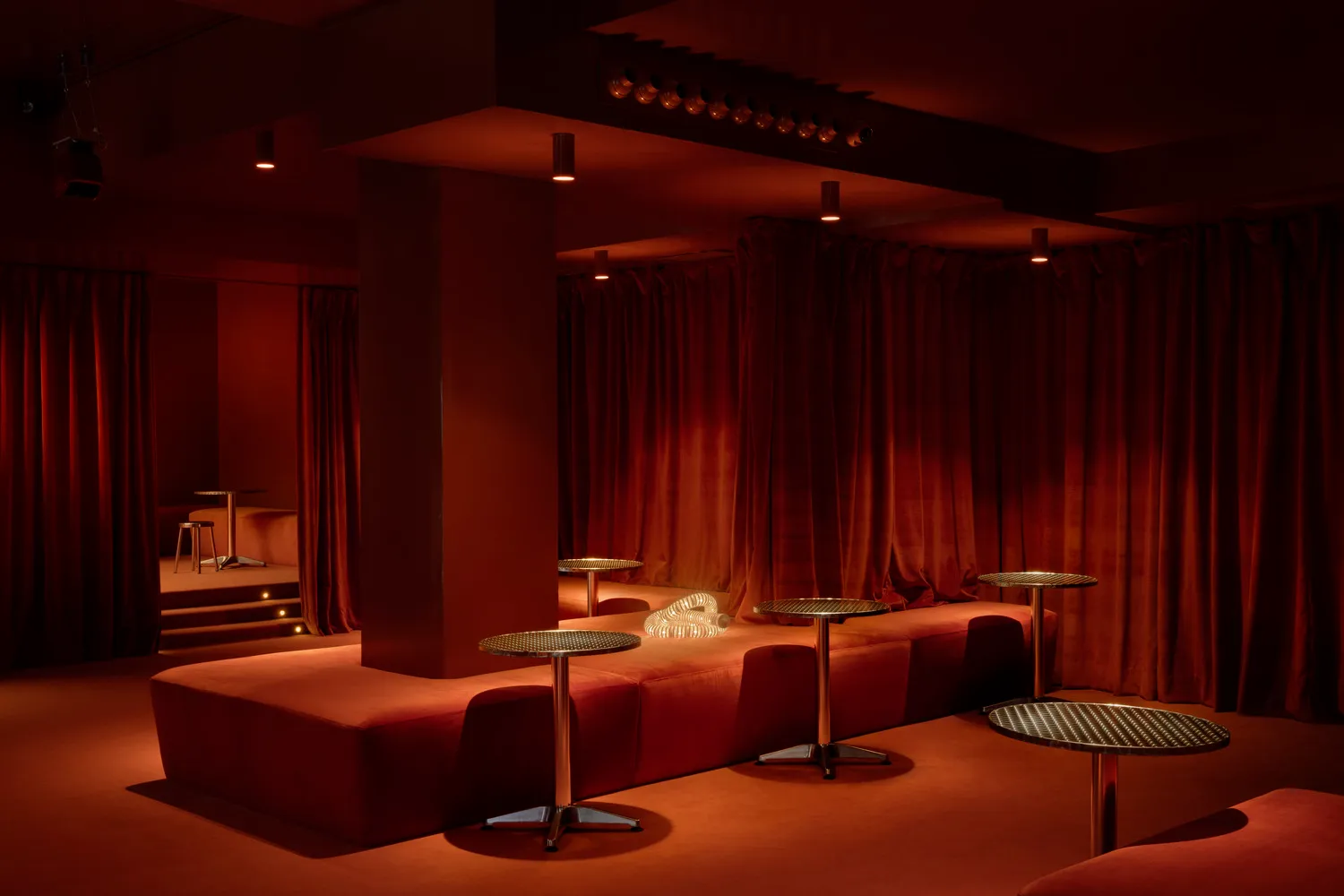 A modern nightclub interior featuring plush red velvet seating and illuminated tables, with a focus on the luxurious and eleg