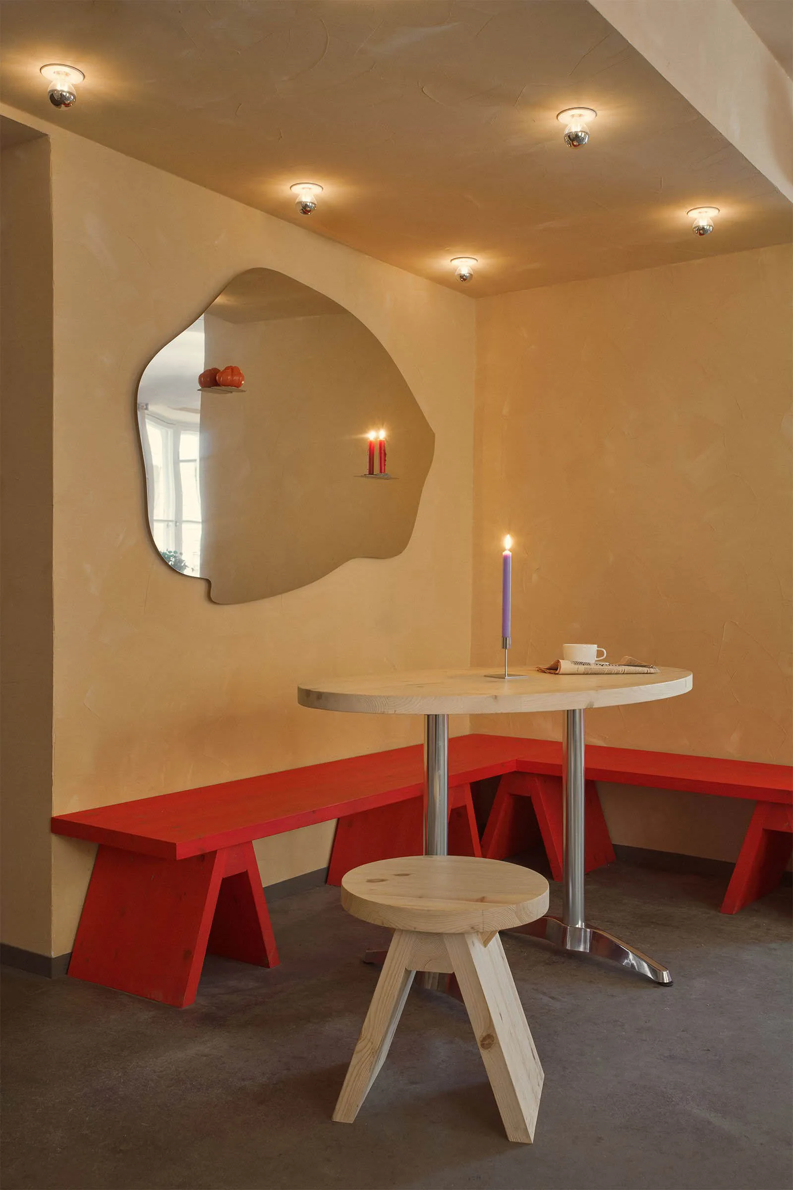 A minimalist restaurant interior featuring a red bench seating area, wooden table, and hanging light fixtures.