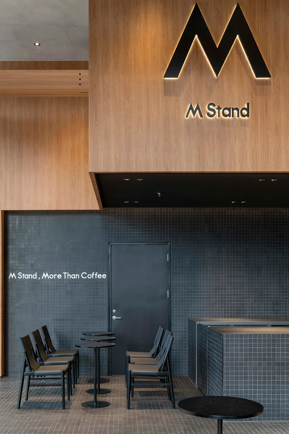 A well-designed modern coffee shop with wooden paneling on the walls, a black counter, and sleek black furniture.