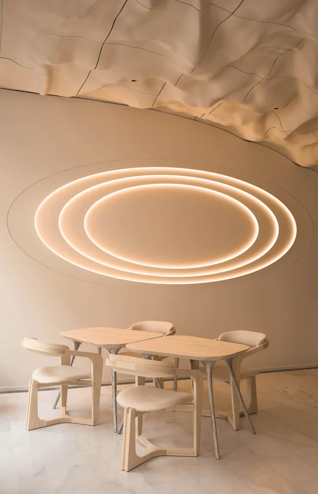 Modern minimalist interior design featuring wooden tables and chairs with a circular light fixture and curved ceiling.