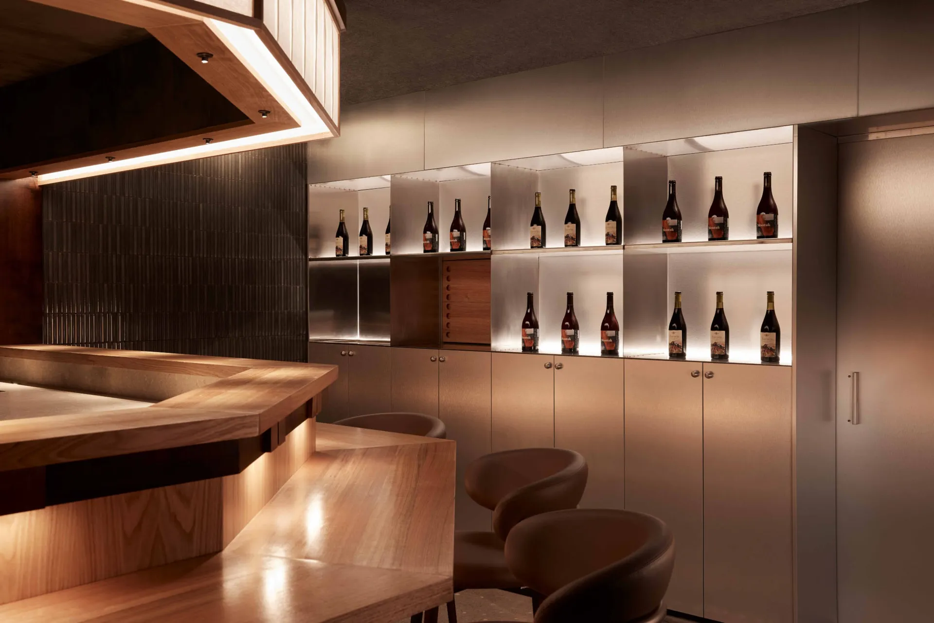 A modern bar interior featuring wooden fixtures, metal shelves, and glass bottles.