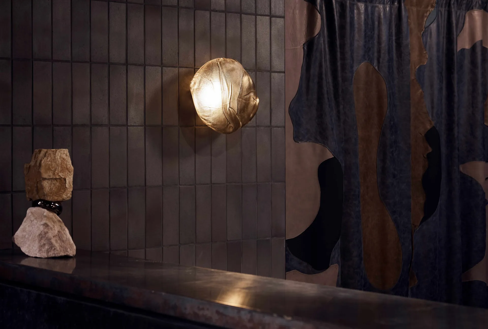 A modern industrial kitchen with metallic elements and a metallic sconce illuminated against a tiled wall.