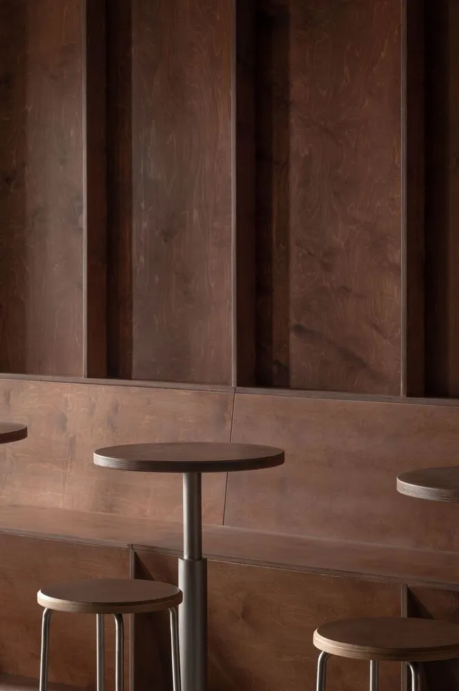 Modern café seating area featuring wooden stools and a round table with a concrete base, set against a wooden paneled wall.