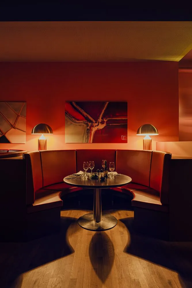 A cozy restaurant interior with red leather booths, a round table, and warm lighting.