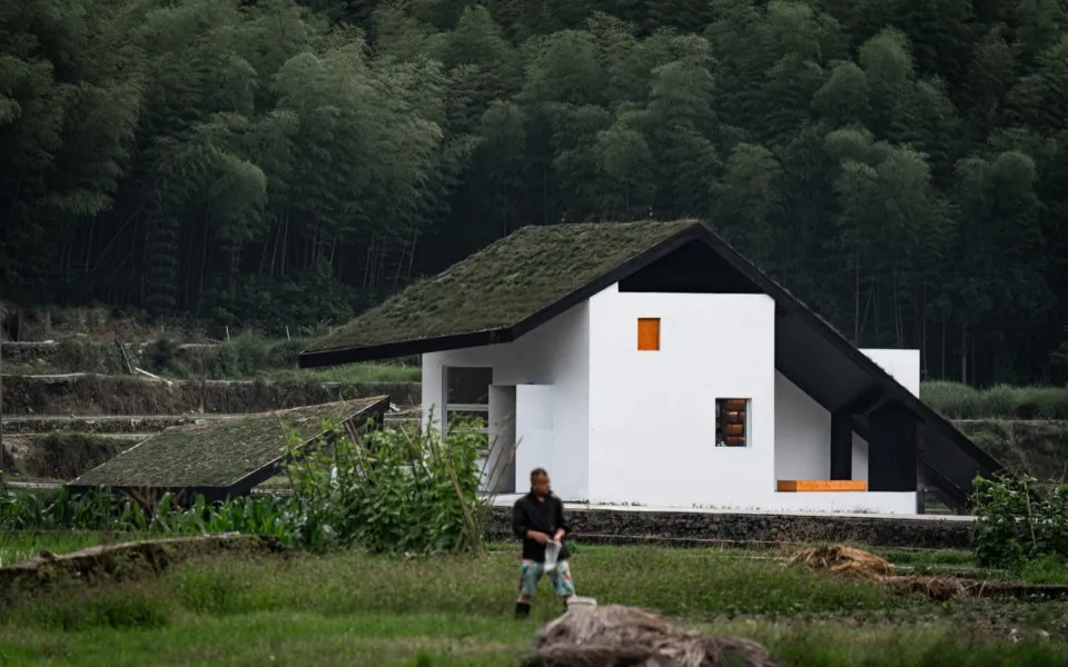 一座極簡建築,擁有混凝土牆面與玻璃屋頂,周圍環繞綠意。