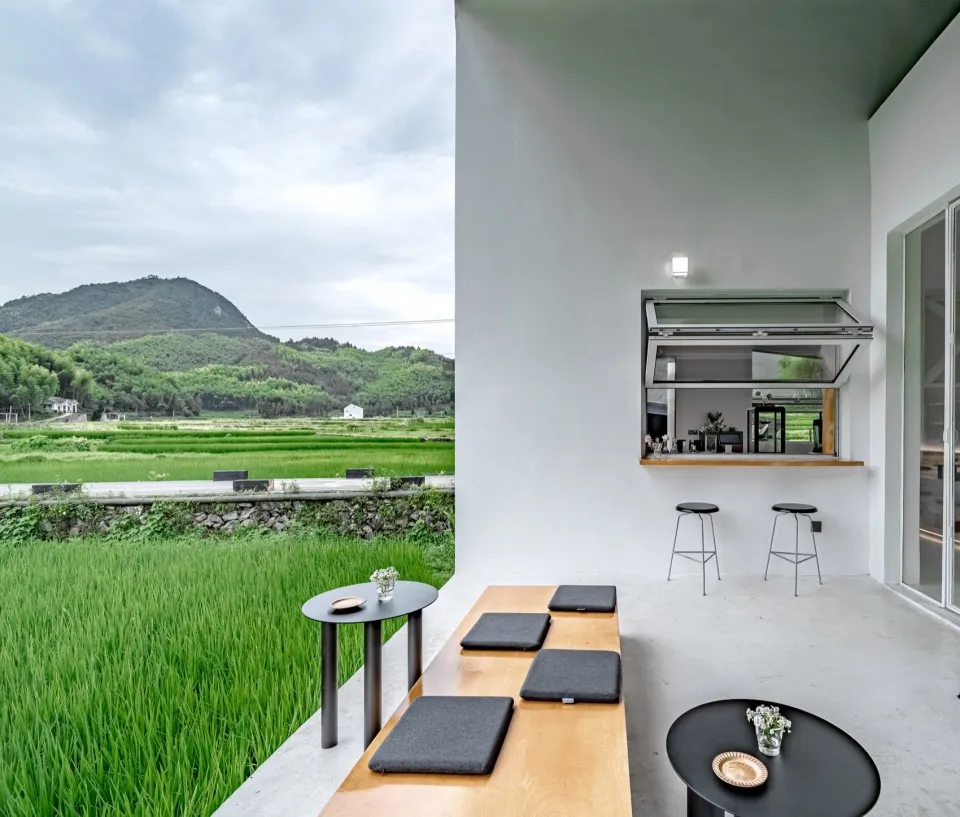 A minimalist outdoor living space featuring a sofa, coffee table, and a view of lush green fields and mountains.
