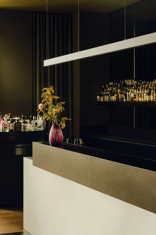 A sleek, modern bar counter with a glass vase containing flowers, set in a contemporary interior design setting.