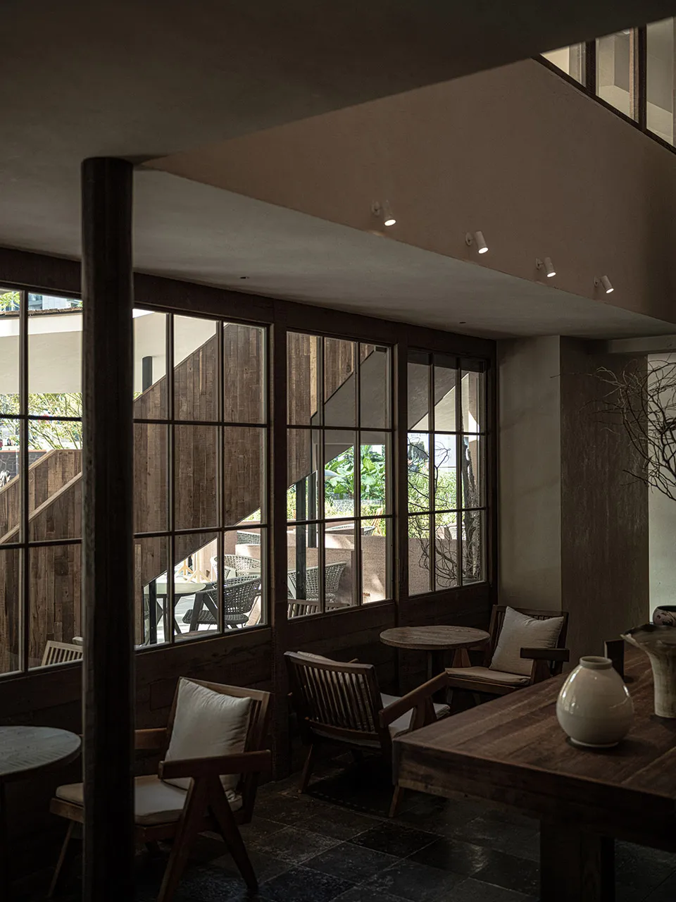An indoor space with industrial design featuring wooden furniture and walls, glass windows, and comfortable seating options.