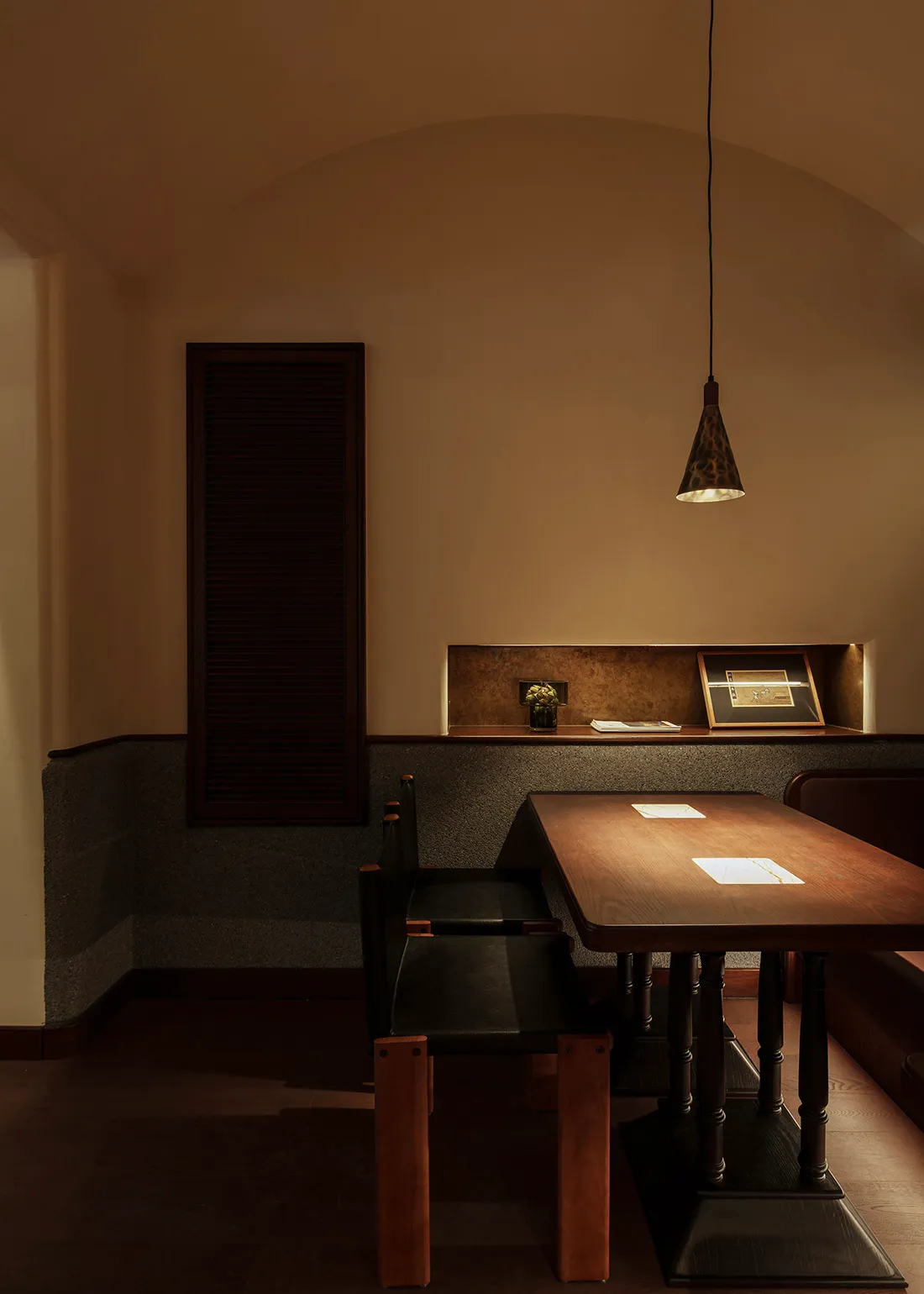 An industrial-style restaurant dining area with a wooden table, black leather chairs, and pendant lighting.