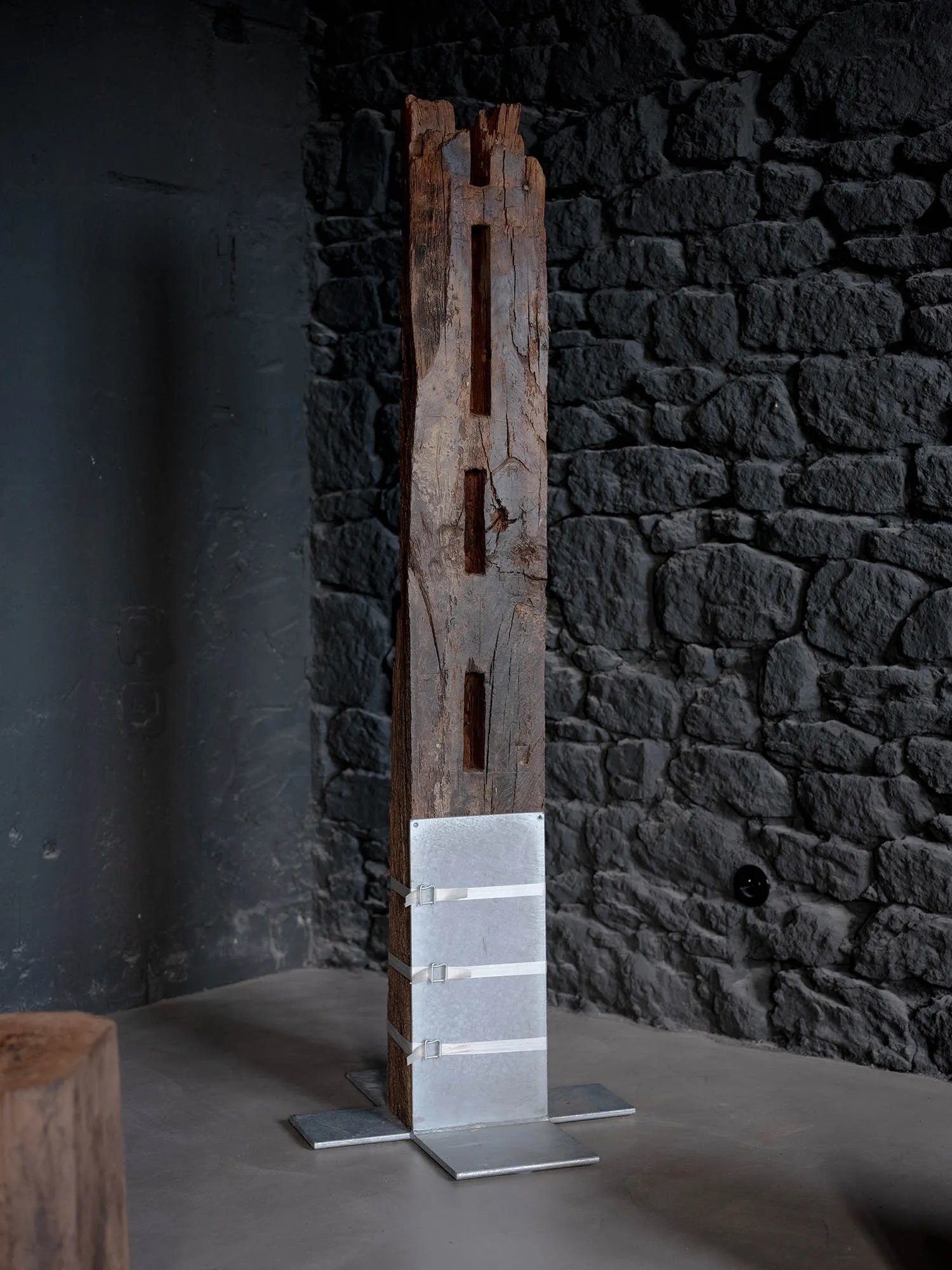 A tall, vertical industrial object made of metal and wood, mounted on a metallic stand.