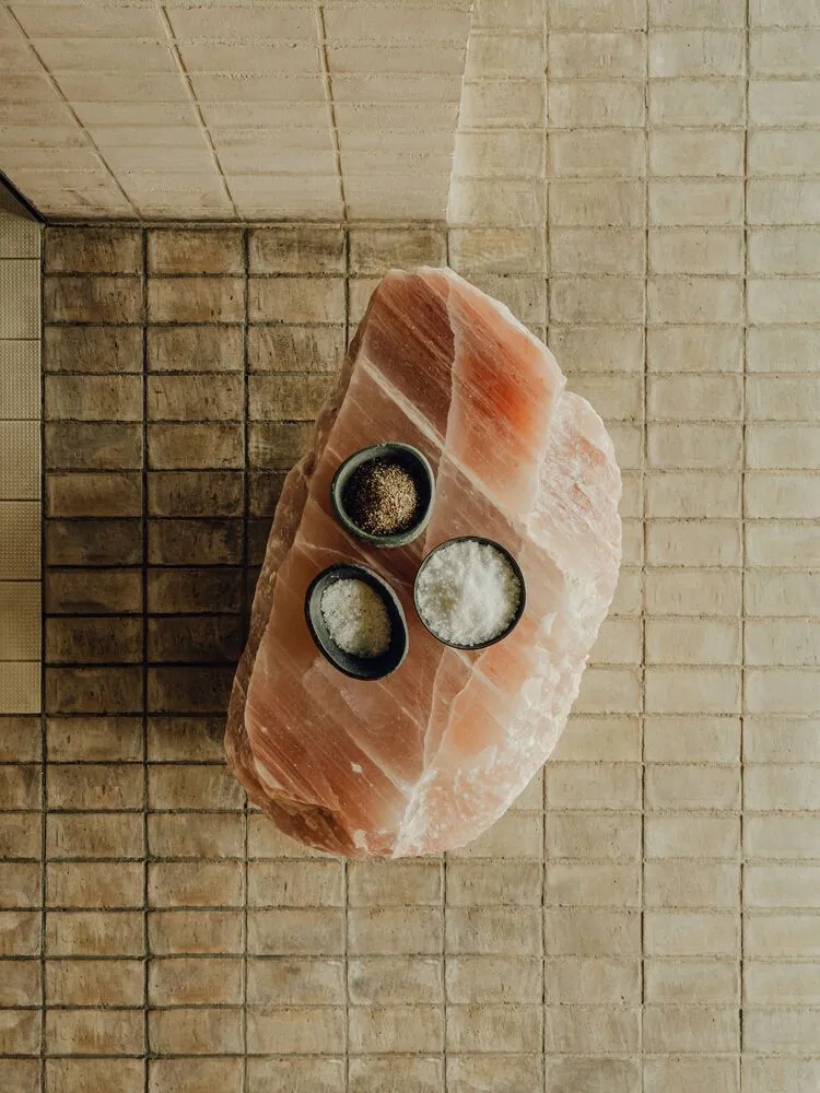 A minimalist kitchen with a large, raw stone slab featuring three small bowls containing different types of spices.