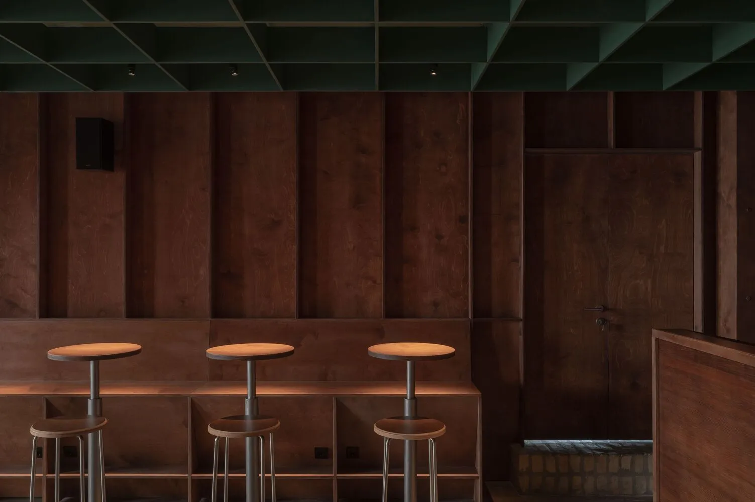 A minimalist bar area with a modern design featuring wooden and metallic surfaces and industrial stools.