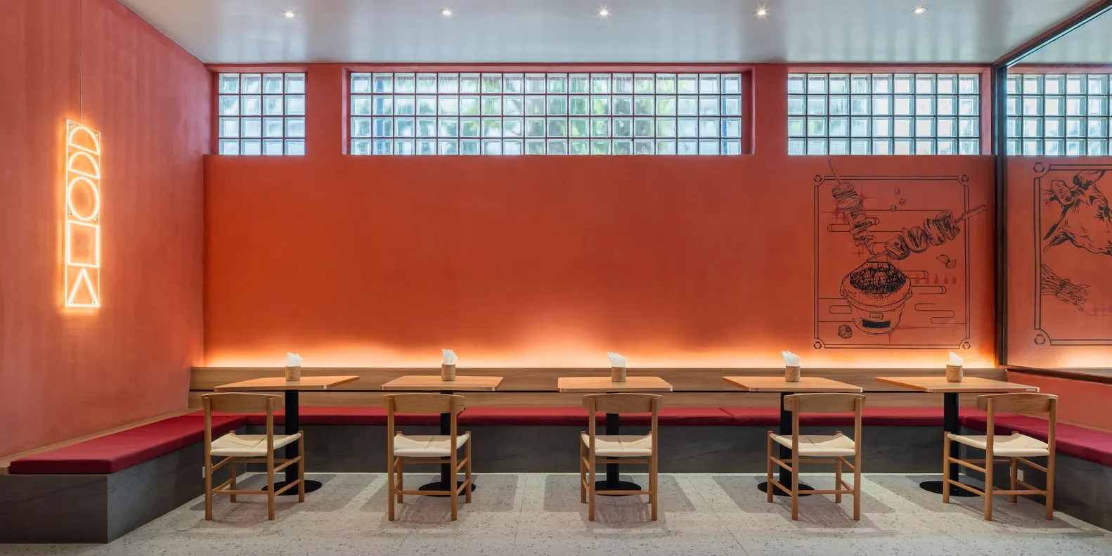 A modern restaurant interior with concrete walls, glass block windows, and wooden tables and chairs.