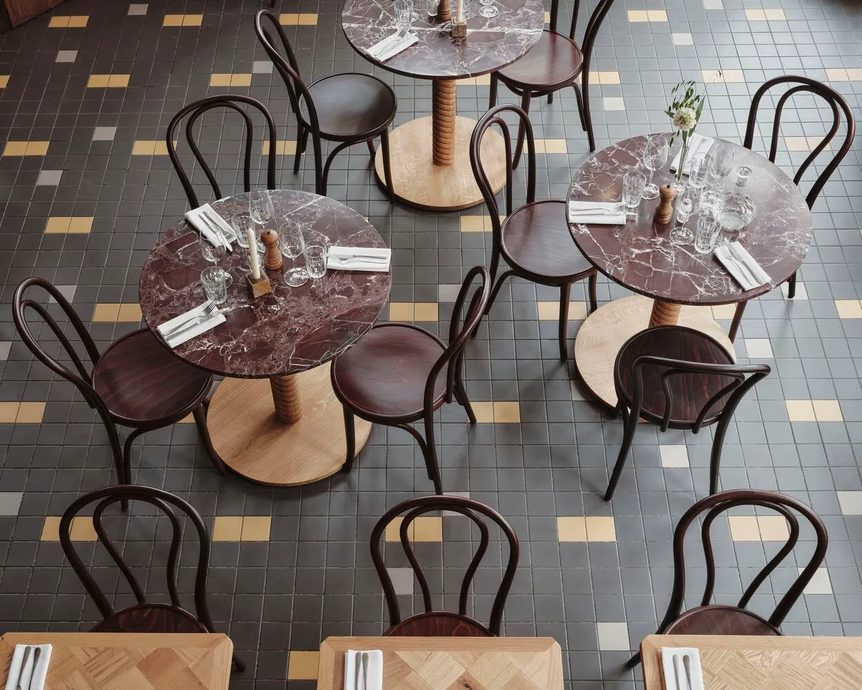 A modern restaurant with round marble tables and wooden chairs.