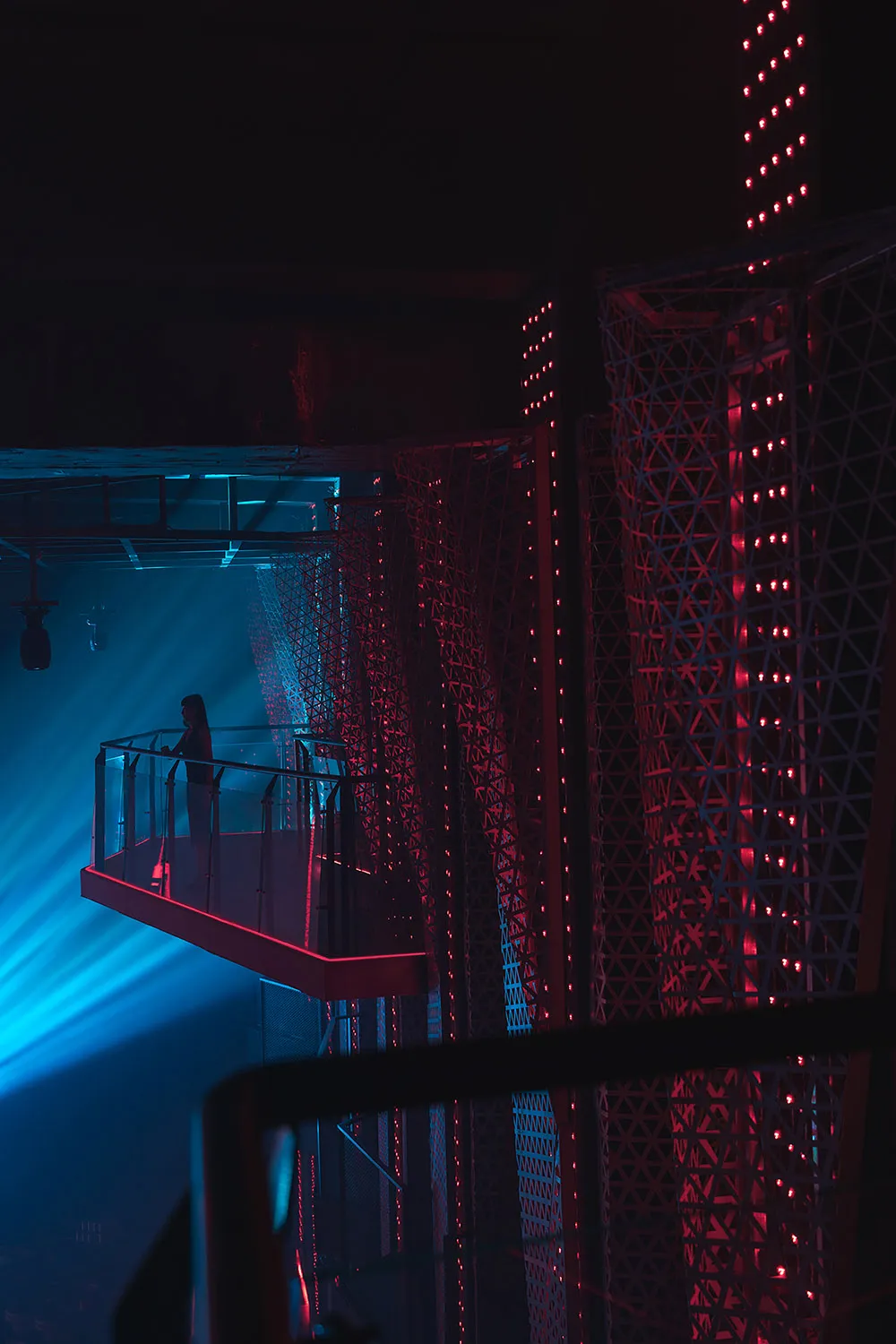 A sleek, industrial-themed concert platform illuminated by red and blue lights with a person standing on it.