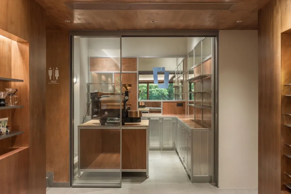 A modern coffee shop kitchen featuring metal cabinets and a glass wall.