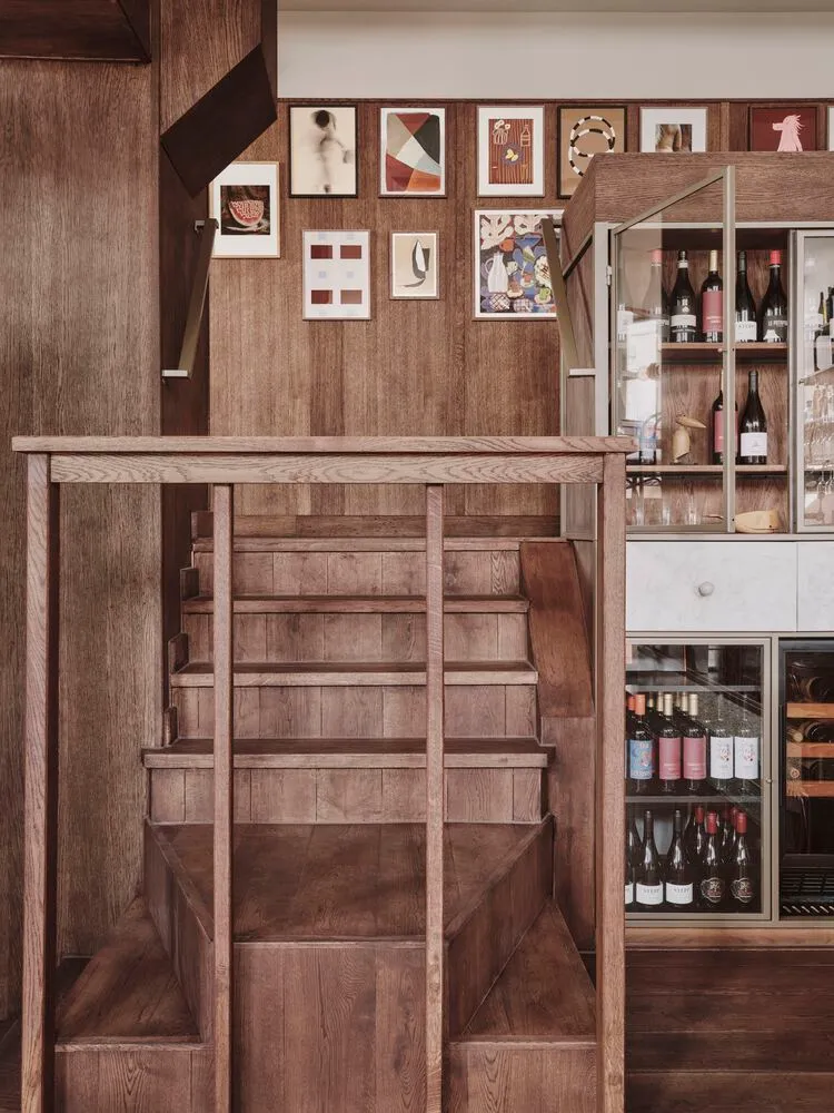 A wooden bar counter with a staircase leading to another level and a wine rack with bottles.