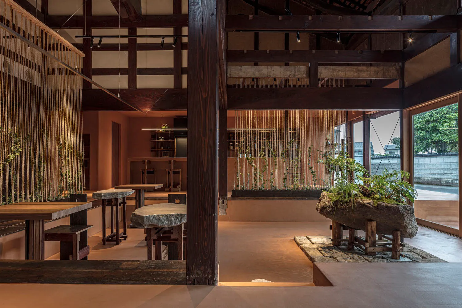A spacious modern restaurant interior with wooden beams and tables adorned with plants.