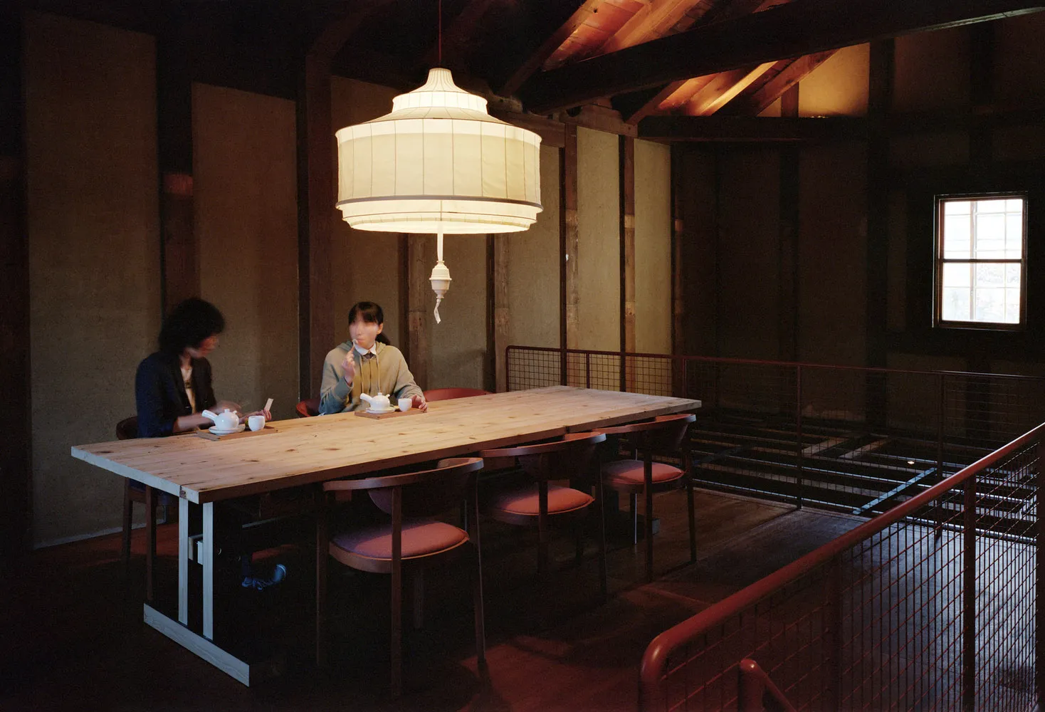 Two people sitting at a wooden table with traditional Japanese interior design elements, including a large hanging lantern.