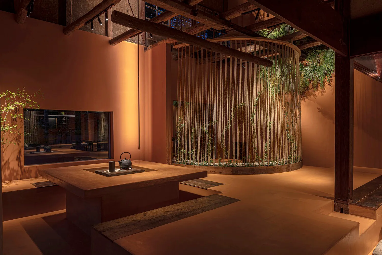 Industrial interior space with wood furniture, ceiling beams, and a central plant wall.
