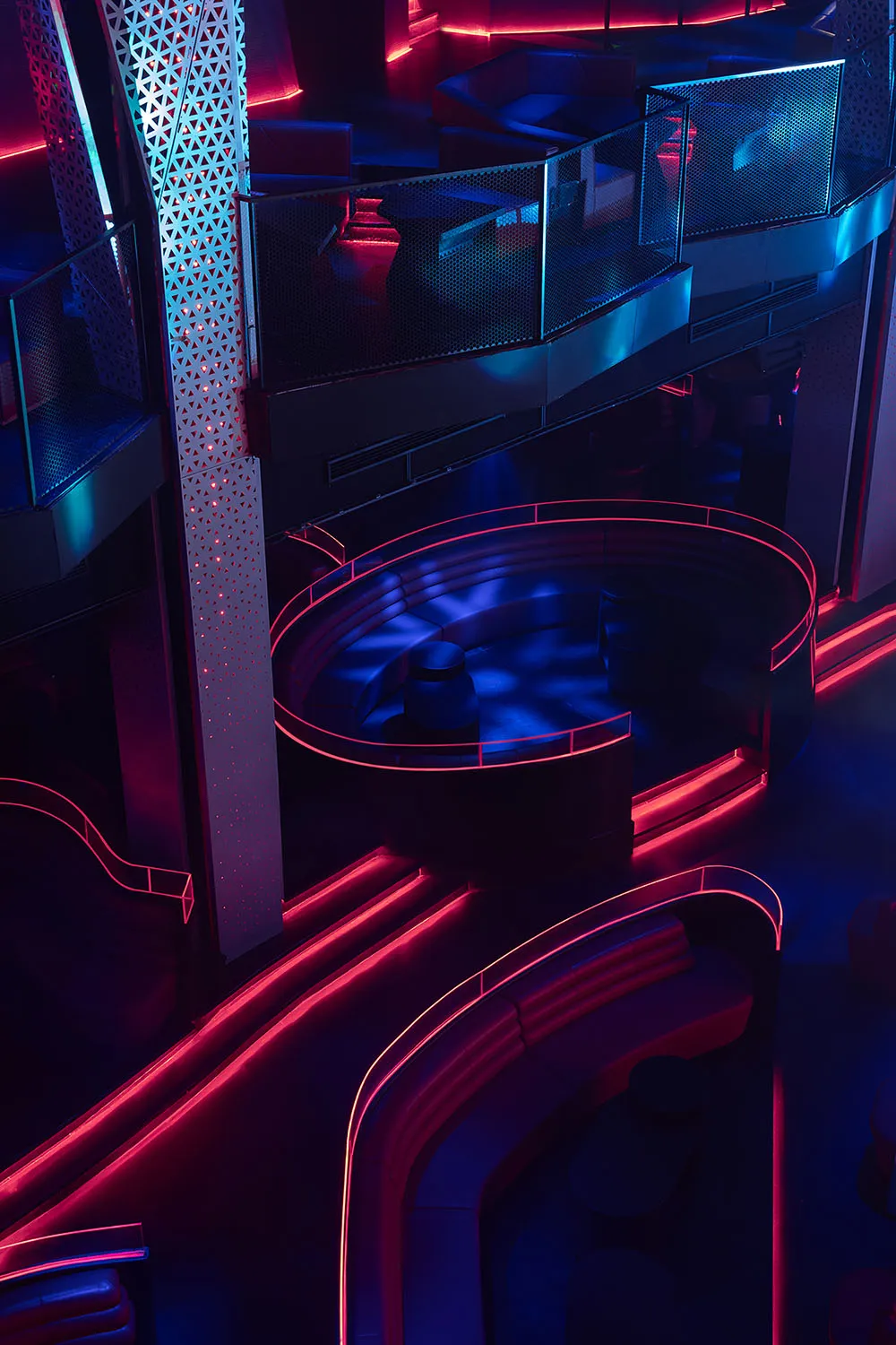 Modern nightclub interior with metallic and plastic seating, illuminated by LED lighting, featuring a concrete floor.