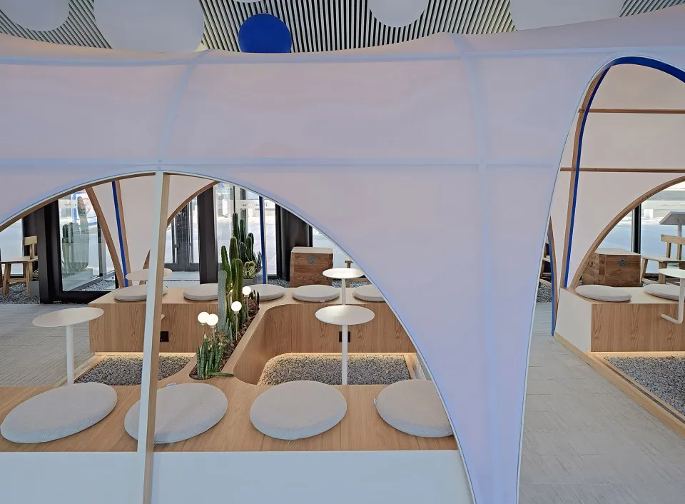A modern industrial restaurant lobby with cushioned seating, a cactus centerpiece, and high ceiling.