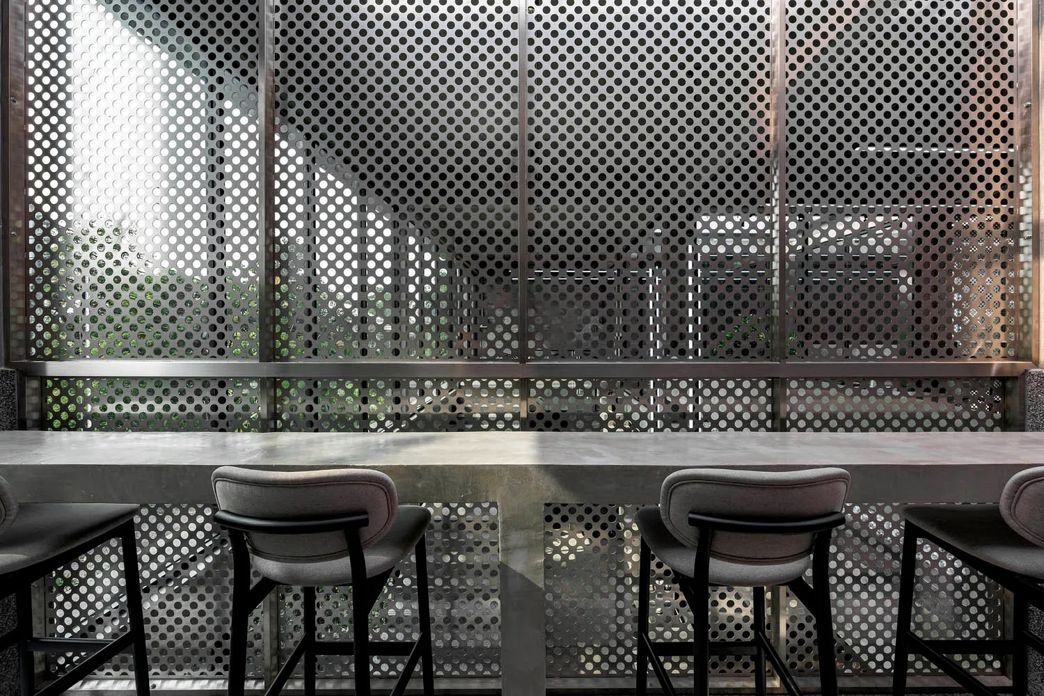 Modern restaurant bar featuring a concrete countertop, stools, and a perforated metal back wall.