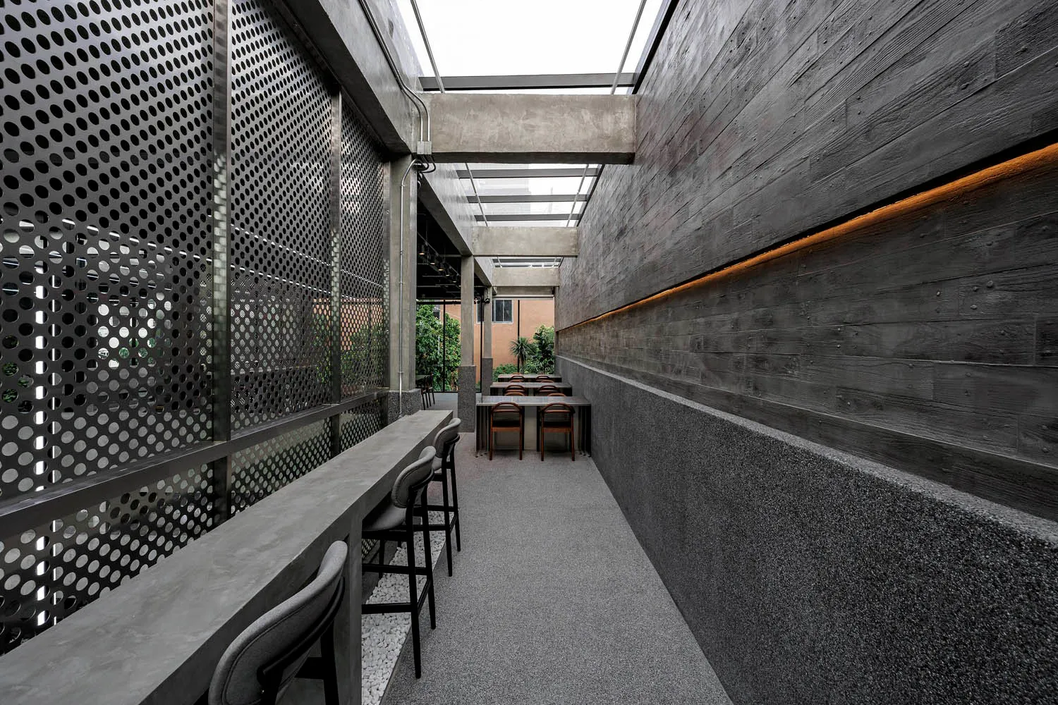 A modern restaurant interior featuring a textured concrete floor and walls adorned with perforated metal panels for light dif