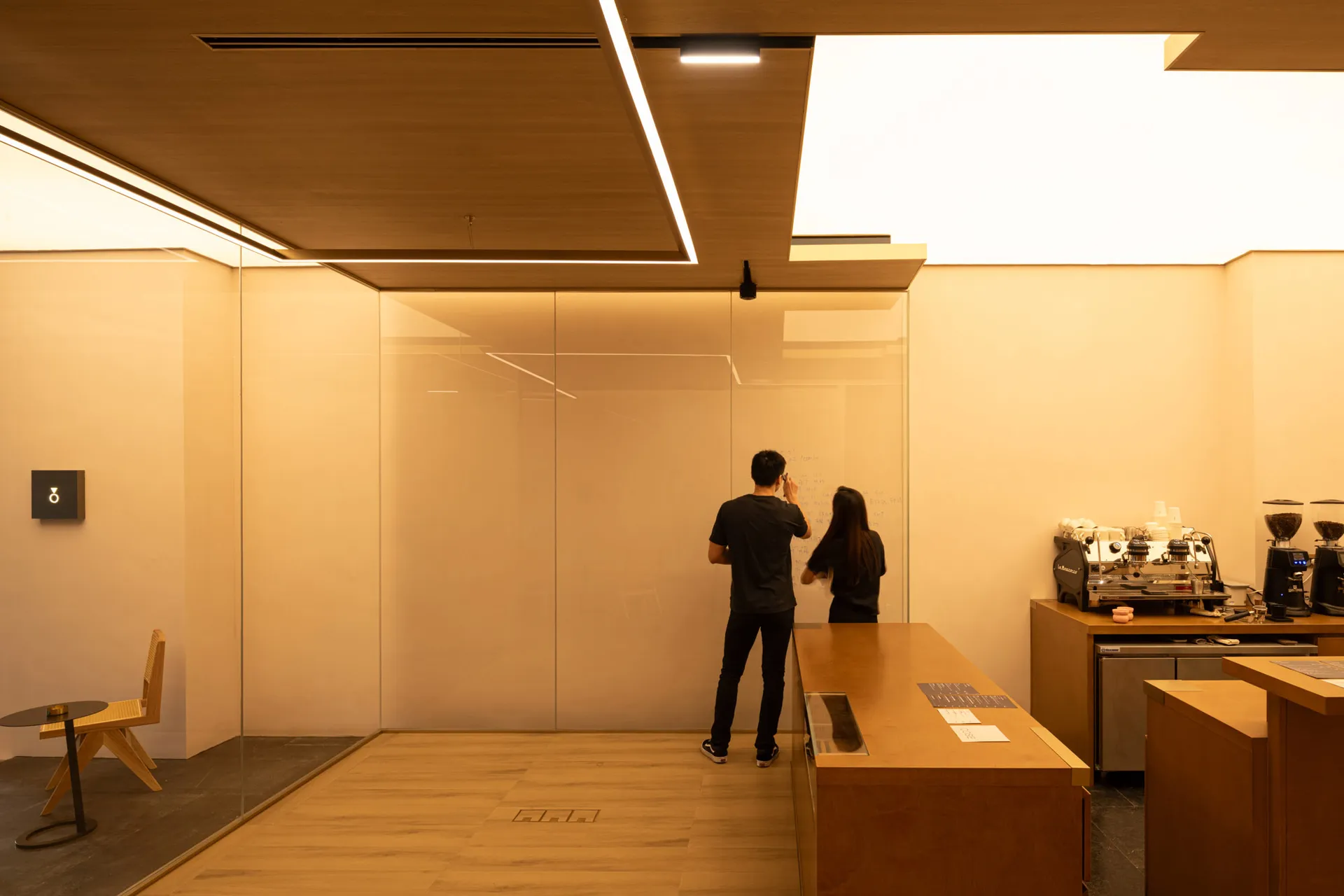 Two people writing on a whiteboard in a modern wooden coffee shop interior.