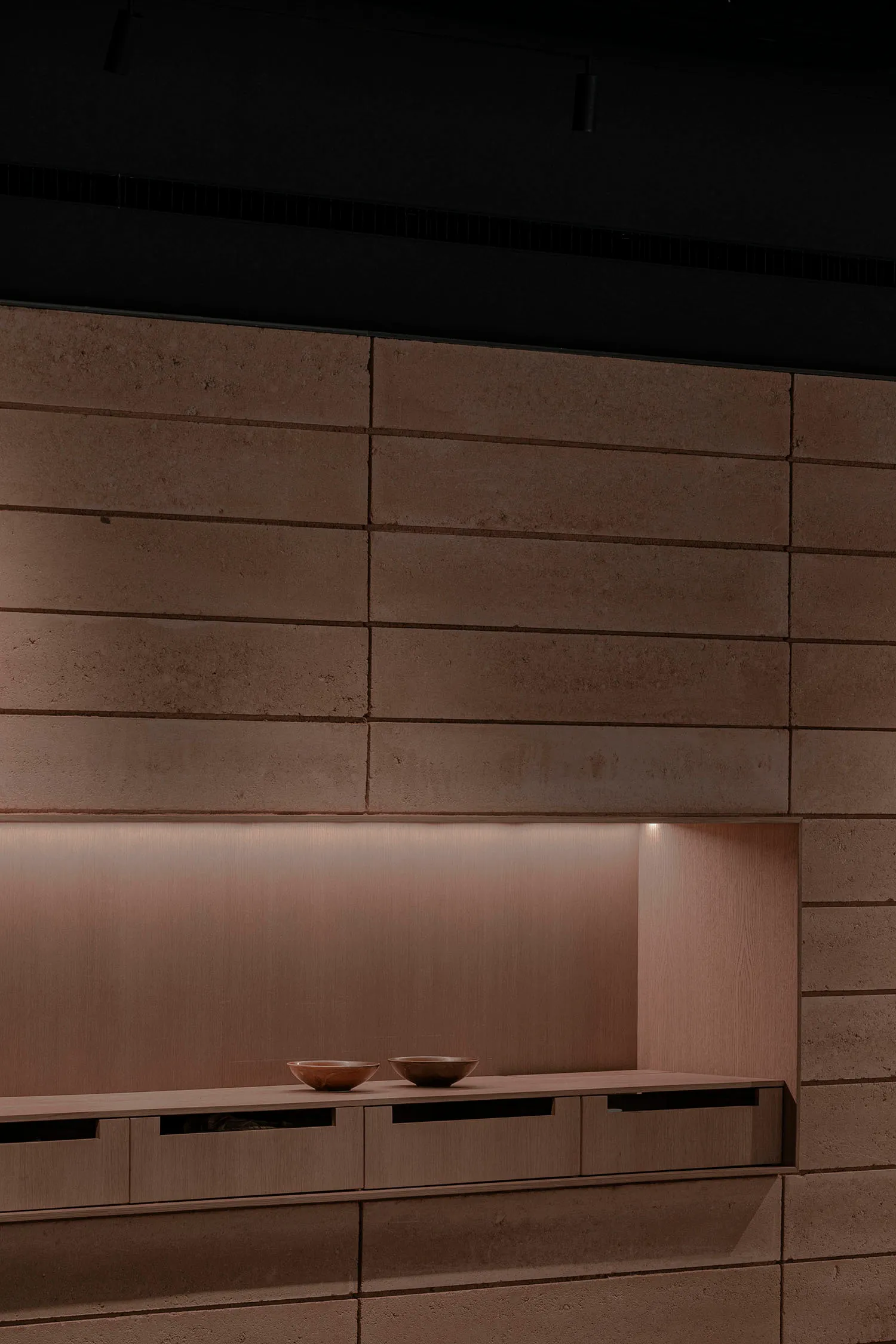 Modern interior space with concrete walls and wooden shelves illuminated by soft lighting.