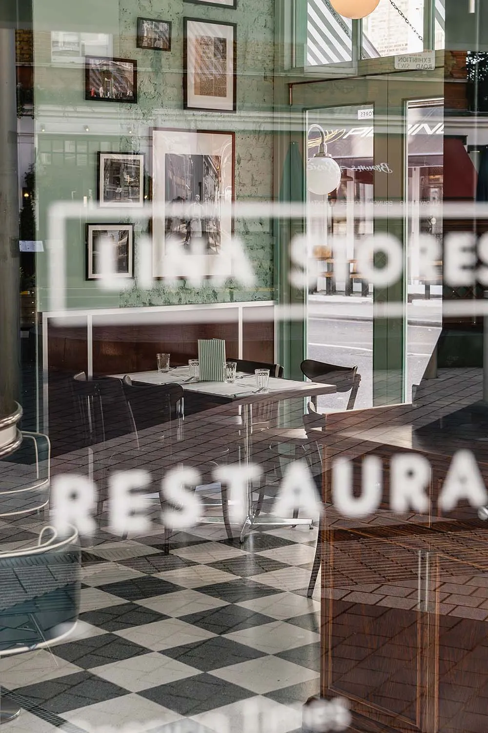 Cafe interior with wooden walls and checkered tiled floor, featuring a dining table and chairs.