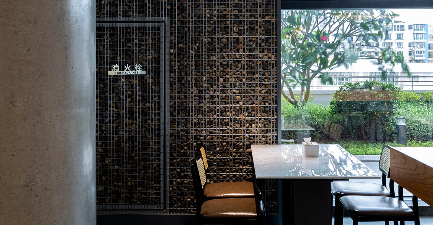 A restaurant interior with a metal grid wall behind a table, featuring pebbles embedded in a concrete wall.