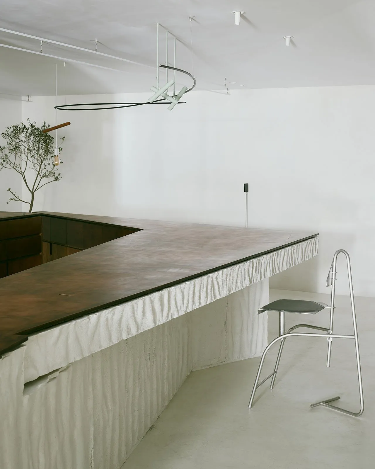 A minimalist modern bar with a concrete countertop and a single metal chair.