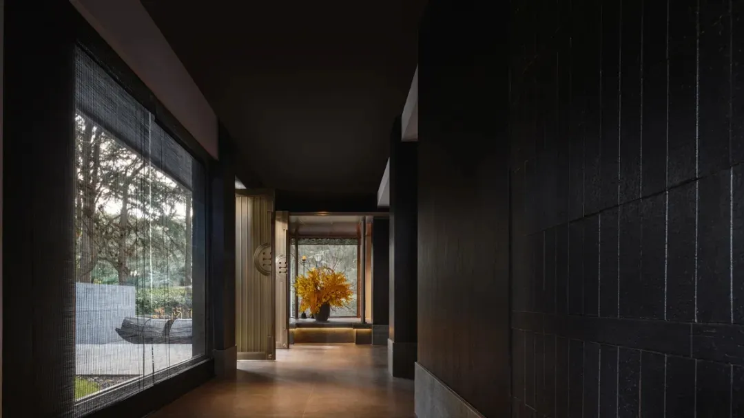 A dark wooden corridor with large windows and a hallway with a vase of yellow flowers.