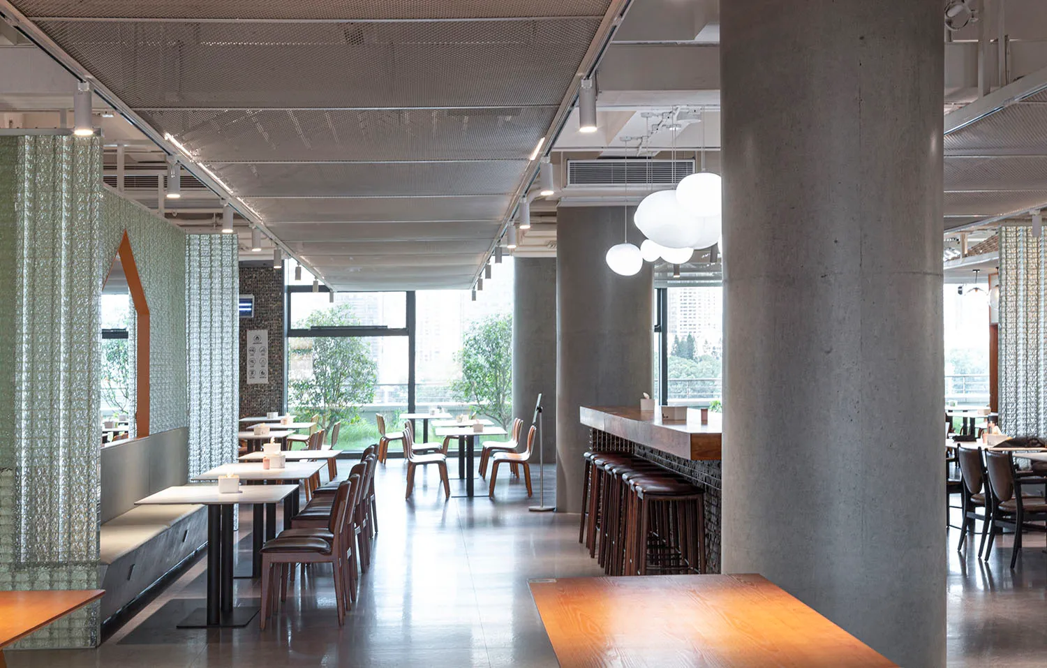 A spacious, modern-industrial restaurant interior featuring concrete, glass, and wooden materials.