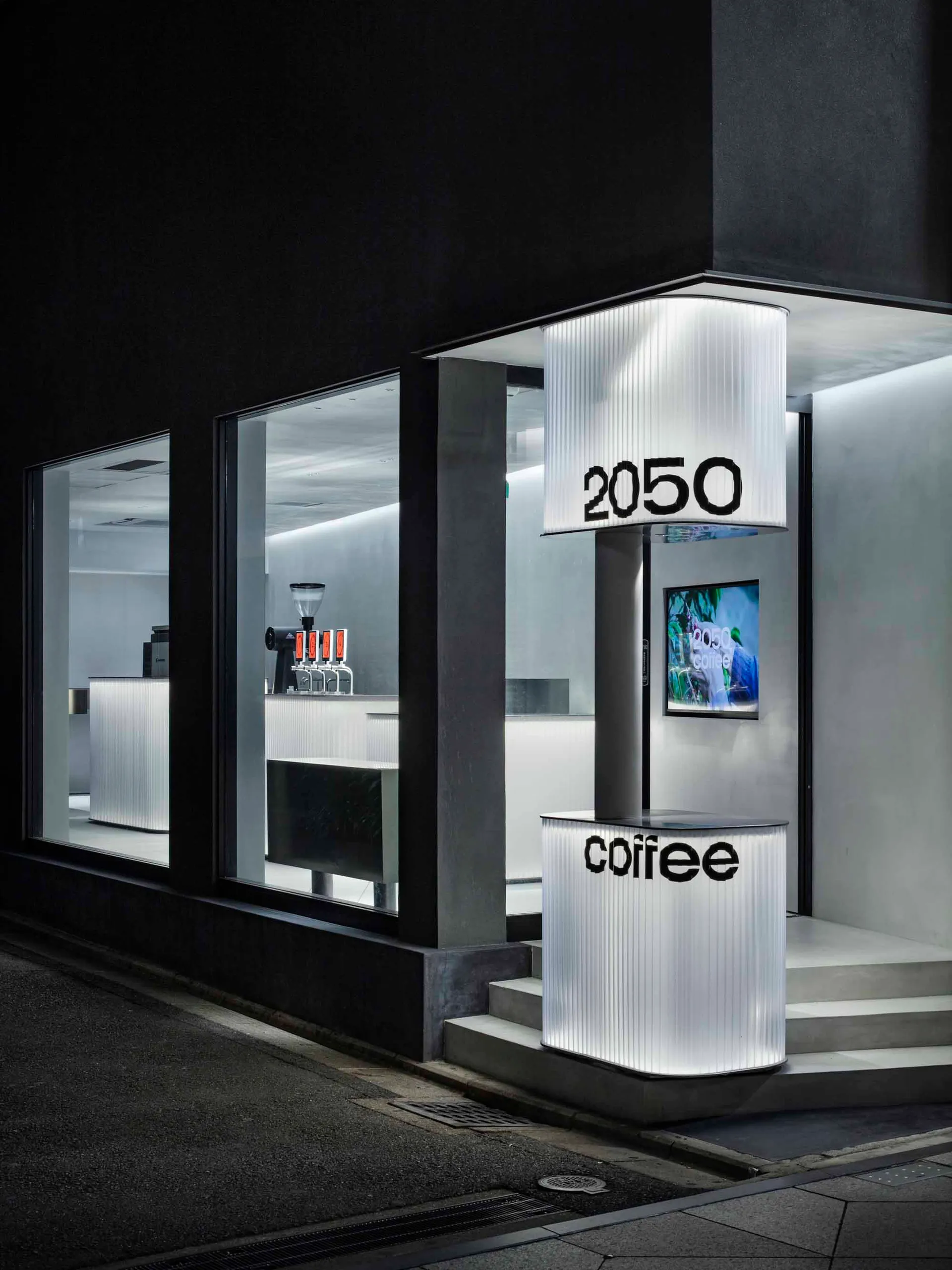 A minimalist coffee shop exterior with a metal exterior, featuring a white sign with black text displaying 'coffee' and '2050