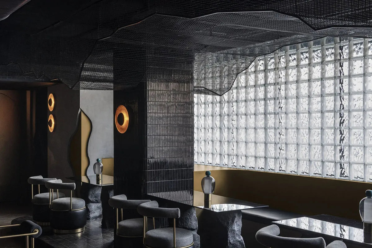 Modern interior design featuring a cafe-bar area with glass brick walls, concrete surfaces, and contemporary lighting fixture