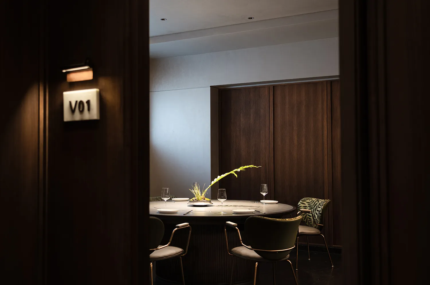A modern, private dining room with wooden walls, a round table, and green chairs.