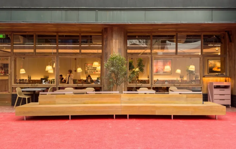 A modern restaurant interior with wooden seating, glass wall, and carpet floors.