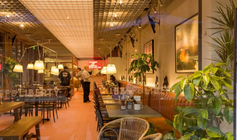 Interior of a restaurant with wooden tables, leather booths, and bohemian decor elements.