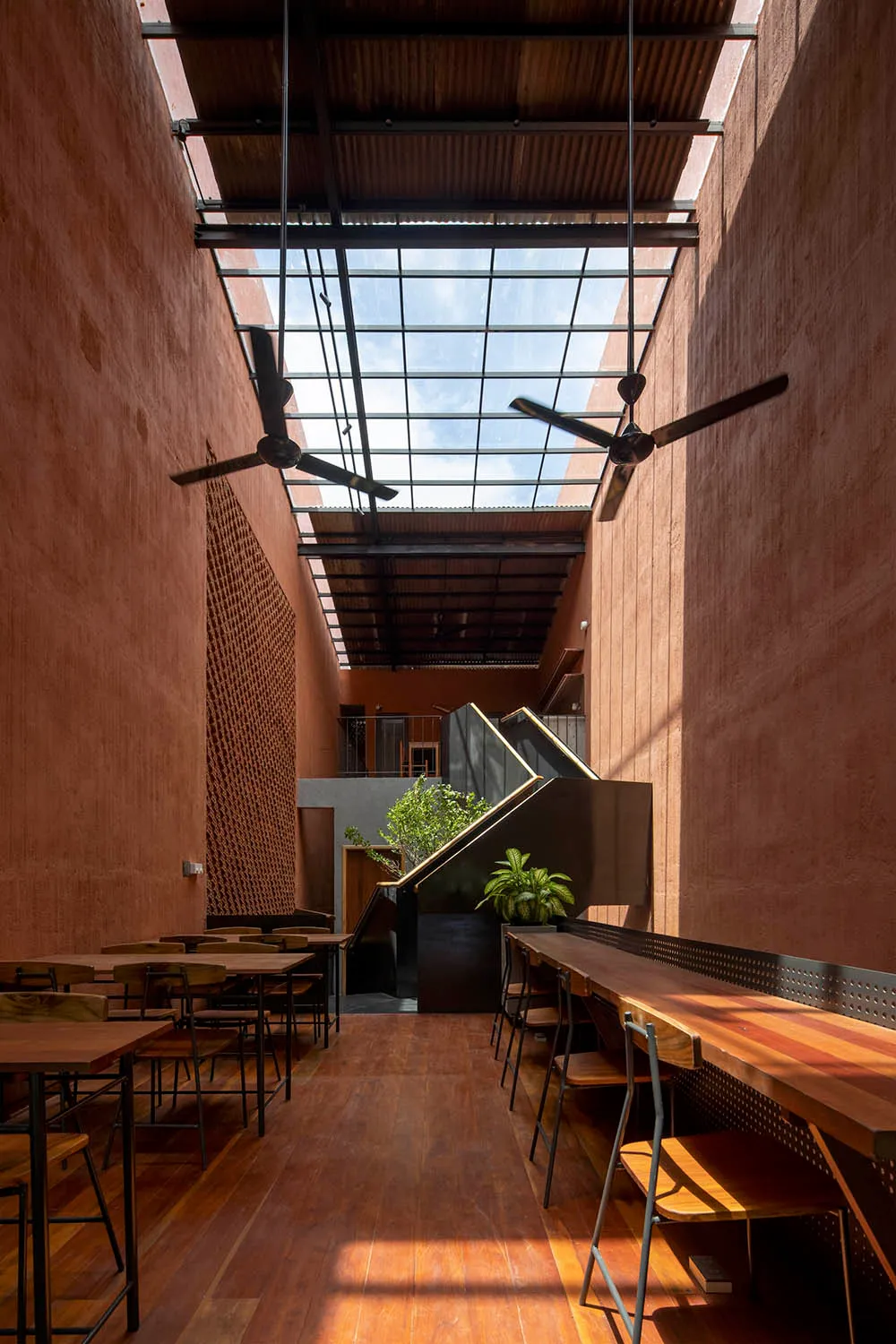 工業風餐廳室內，搭配木製餐桌與陶土色牆面，並設有玻璃天花板面板。
