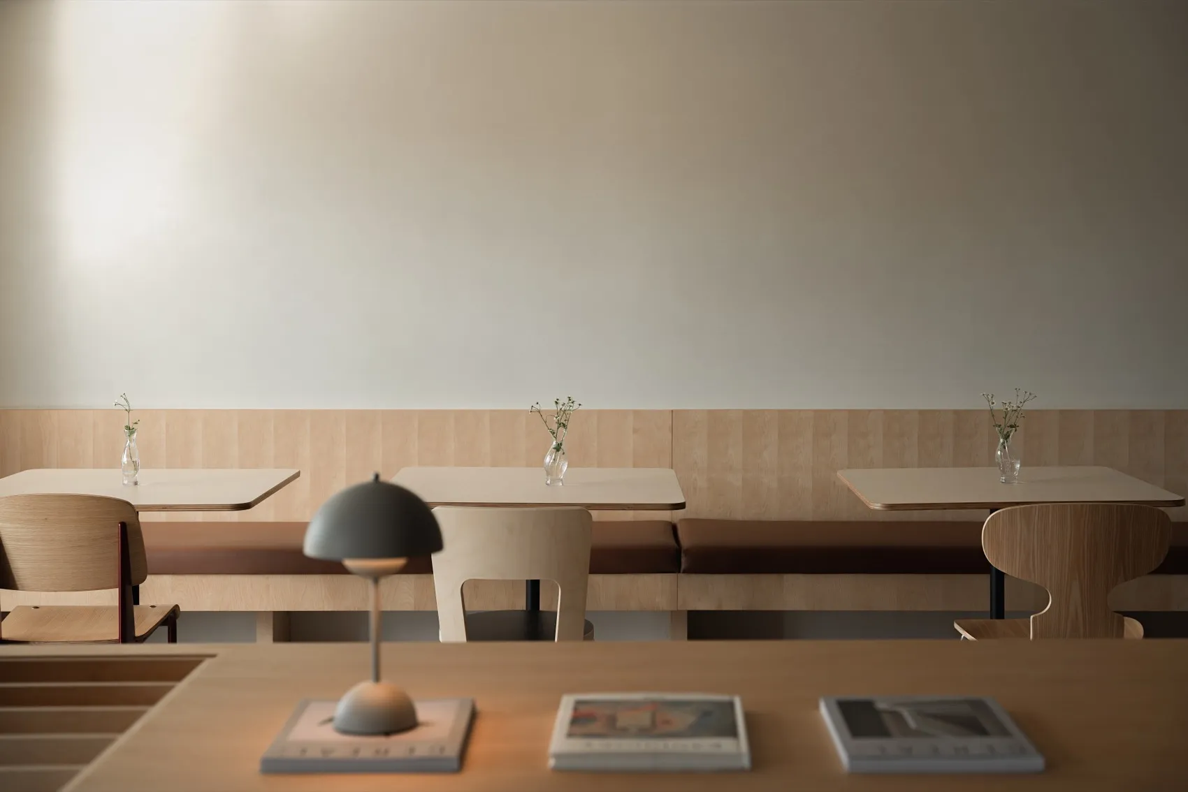 A modern restaurant with minimalist design, wooden seating, and small flower arrangements.